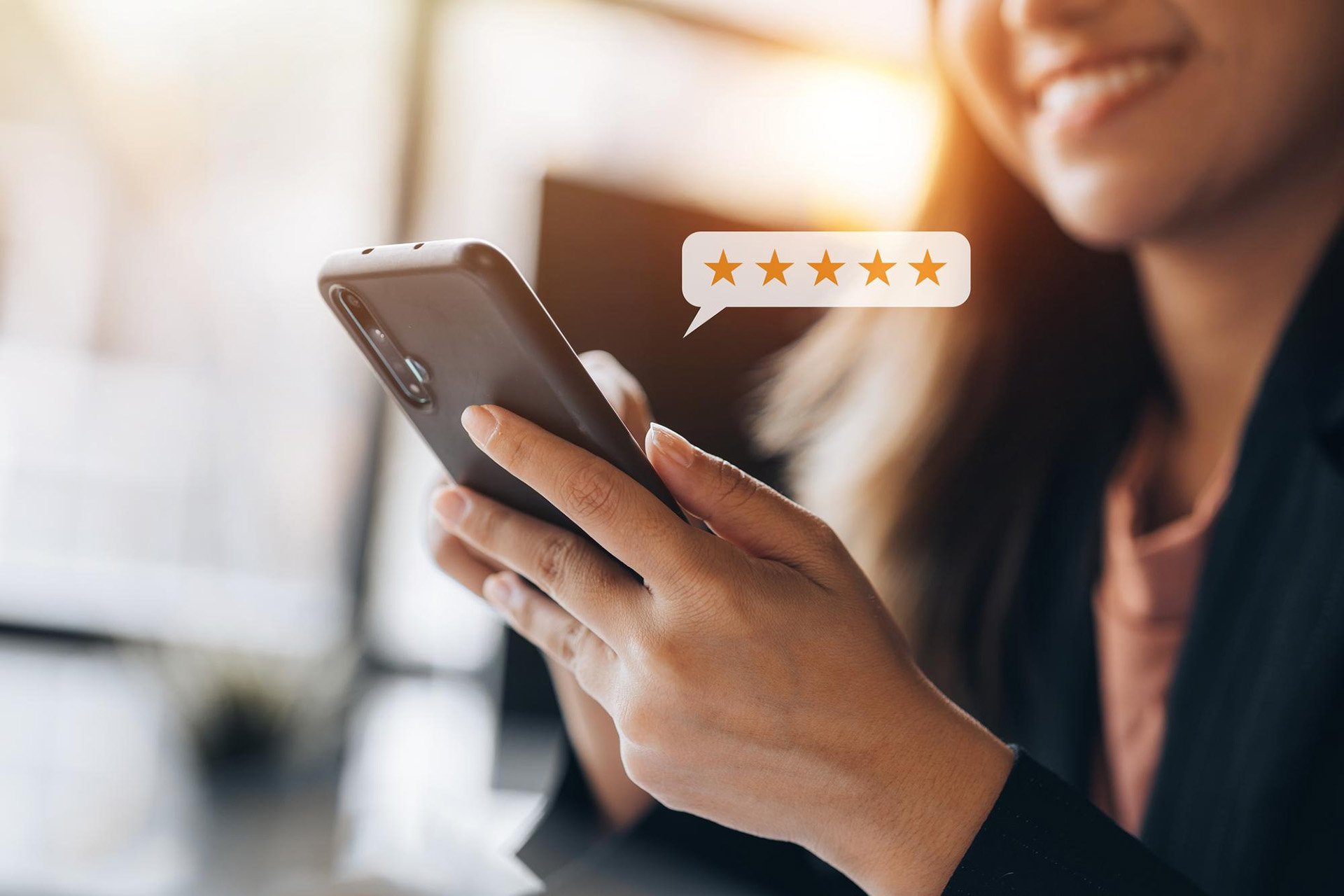 A smiling woman writing a 5 star review on her phone