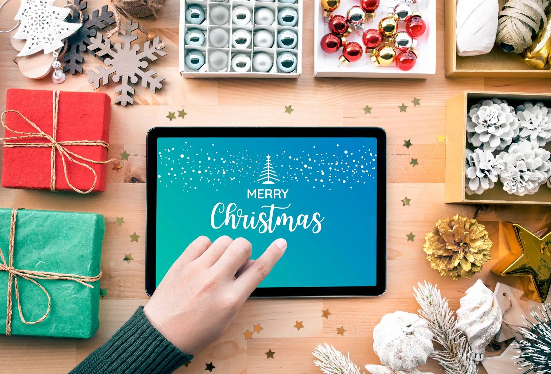 Someone clicking on a Christmas tablet with Christmas decorations around