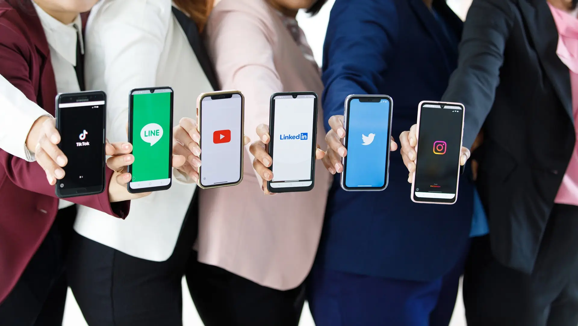 A group of friends wearing formal attire showing their phone screens with different social media platforms on each