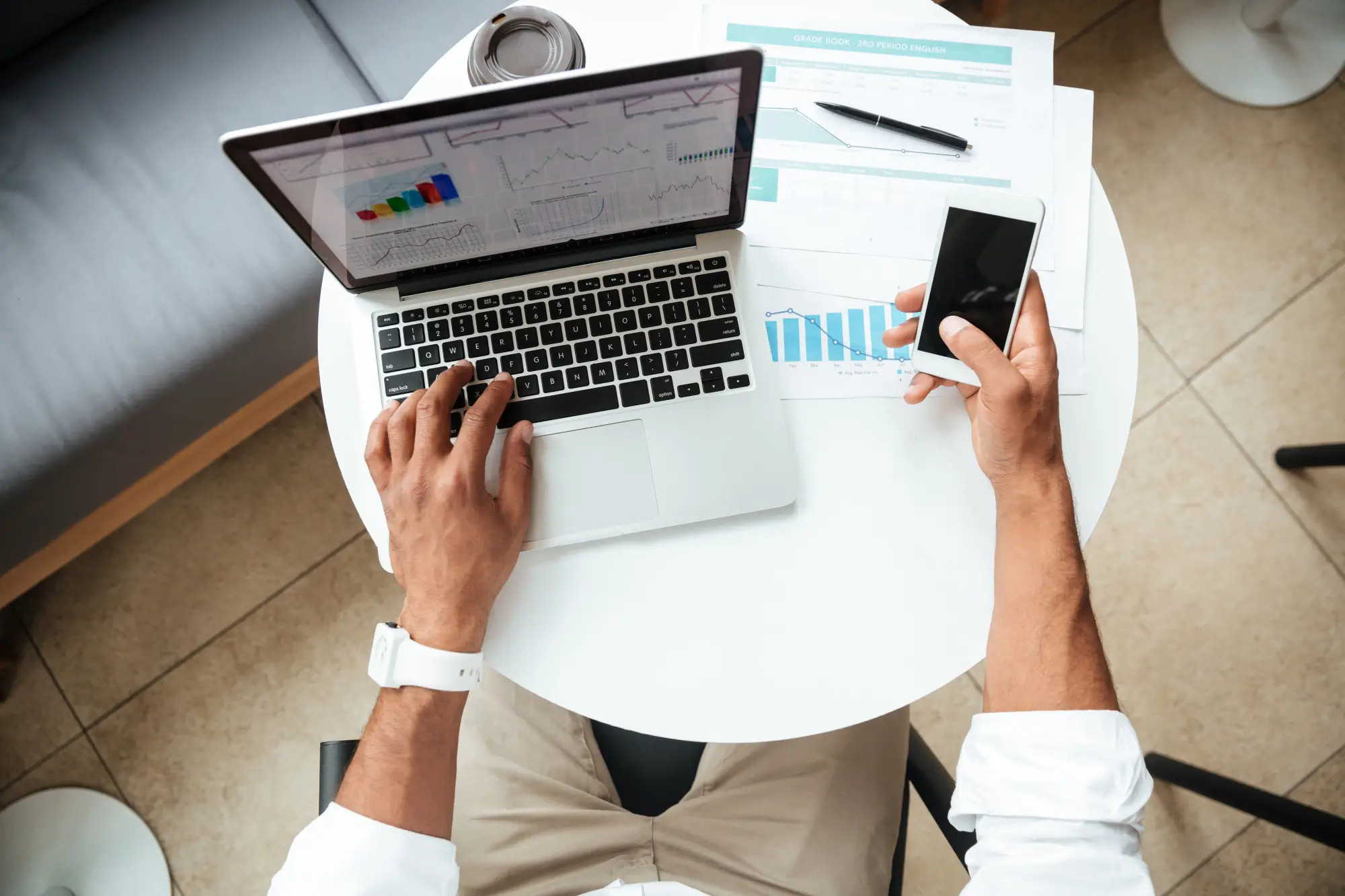 Top down view of a man working on his laptop and phone with papers everywhere