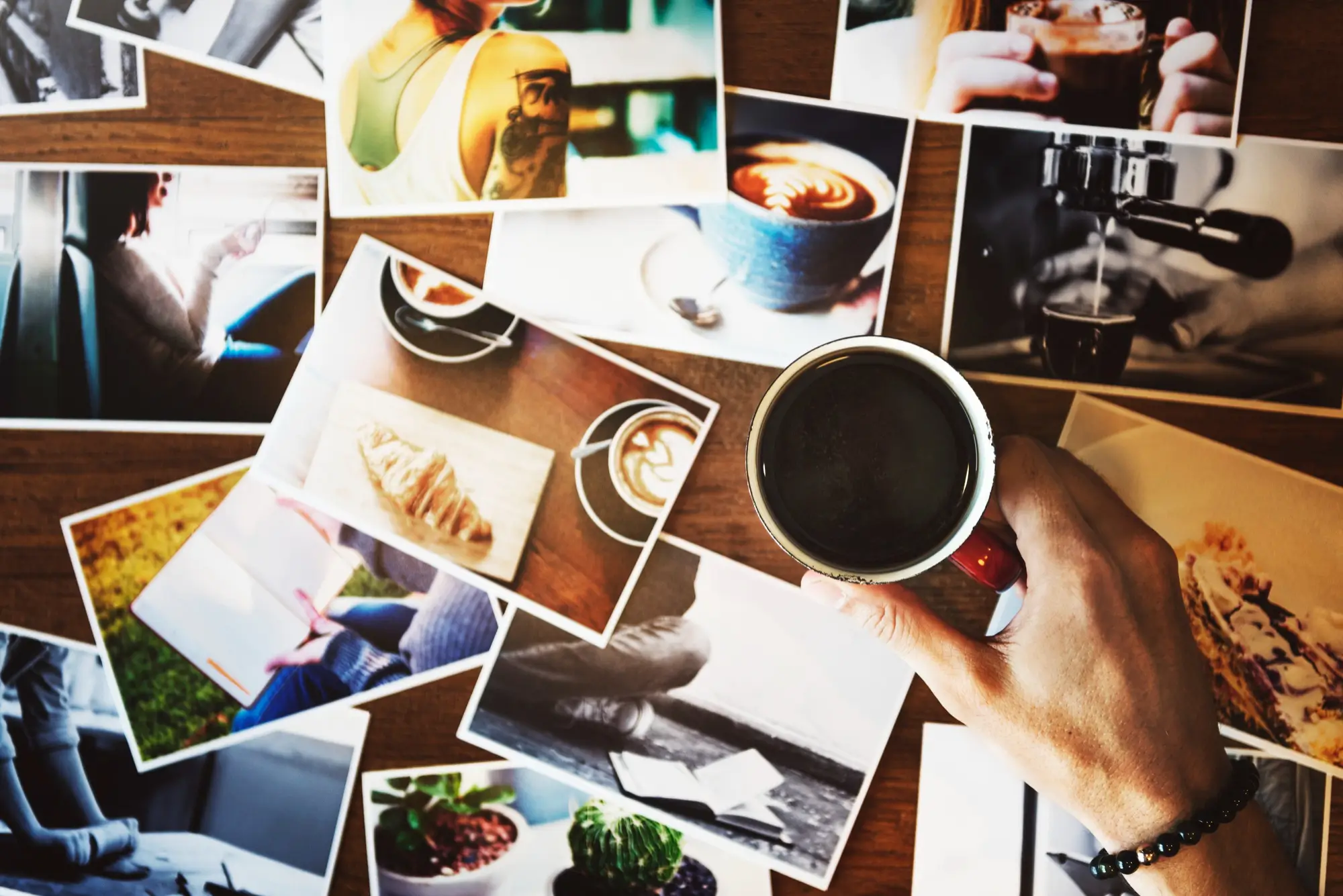 Hand holding coffee cup with photographs on a table