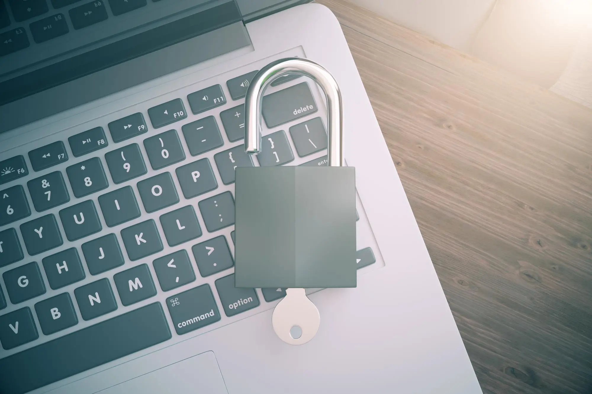 An unlocked padlock with a key on top of a laptop